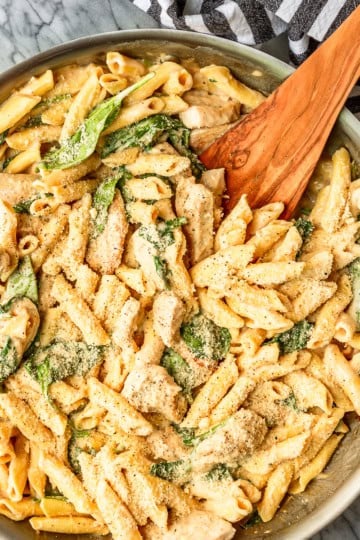 chicken spinach alfredo pasta recipe in a skillet with a black and white striped towel wrapped around the handle