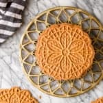 chocolate pizzelle on a gold trivet with a black and white kitchen towel