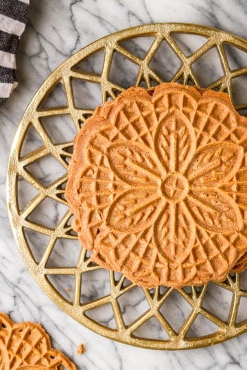 chocolate pizzelle on a gold trivet with a black and white kitchen towel