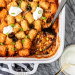 taco tater tot casserole recipe in a white ceramic baking dish with sliced green onions and black olives on the side