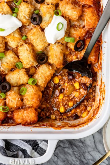 taco tater tot casserole recipe in a white ceramic baking dish with sliced green onions and black olives on the side