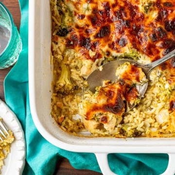 cheesy chicken and rice casserole recipe being scooped out of a white ceramic baking dish with a silver serving spoon