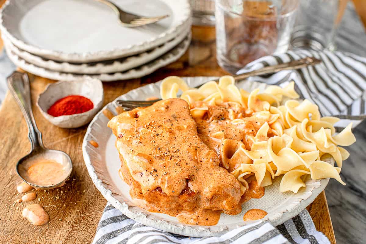 paprika pork chops and sour cream with egg noodles on a white plate