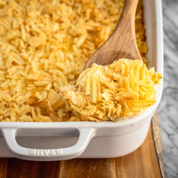 cheesy hashbrown casserole recipe in a white ceramic baking dish with a wooden spoon