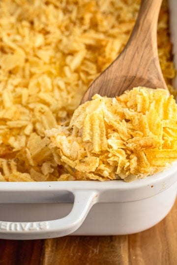 cheesy hashbrown casserole recipe in a white ceramic baking dish with a wooden spoon