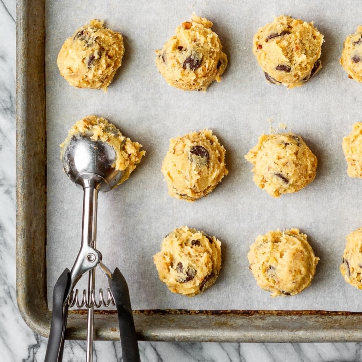 frozen cookie dough balls with a cookie scoop on a baking sheet lined with parchment paper