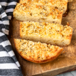 homemade garlic bread recipe on a wooden cutting board with a black and white striped towel