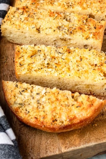 homemade garlic bread recipe on a wooden cutting board with a black and white striped towel