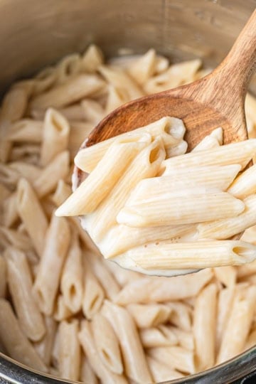 cream cheese pasta sauce being scooped out of an instant pot with a wooden serving spoon