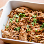 beef barbacoa in a white ceramic casserole dish garnished with chopped cilantro