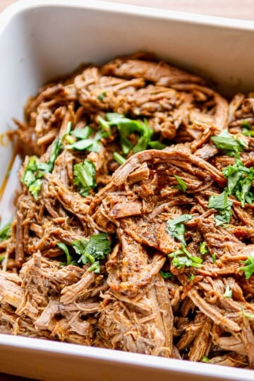 beef barbacoa in a white ceramic casserole dish garnished with chopped cilantro