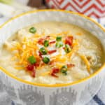 baked potato soup topped with sour cream, shredded cheddar cheese, crumbled bacon and sliced green onions in a ceramic bowl