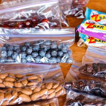road trip snacks consisting of bagged blueberries, grapes, almonds, dried fruit, and granola bars on a wooden table