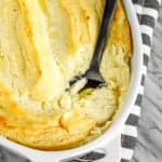 make ahead mashed potatoes in a white ceramic baking dish with a black serving spoon
