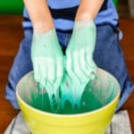 child's hands playing with green oobleck slime in a ceramic bowl