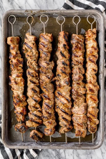 grilled pork kabobs on a metal baking sheet with a black and white kitchen towel