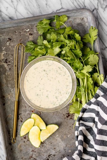 creamy honey garlic lime sauce in a glass bowl with a small gold whisk and cut limes