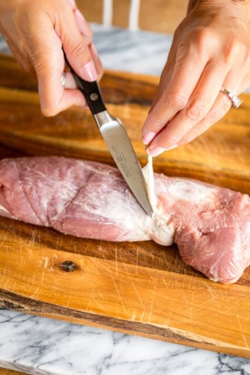 hands holding a paring knife demonstrating how to remove silver skin from pork tenderloin