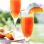 frozen peach bellini in a champagne glass garnished with a fresh peach slice