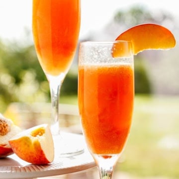frozen peach bellini in a champagne glass garnished with a fresh peach slice