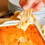 hand scooping buffalo chicken dip out of a baking dish with a tortilla chip