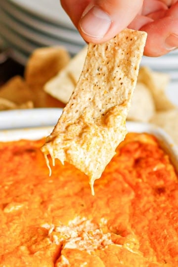 hand scooping buffalo chicken dip out of a baking dish with a tortilla chip