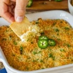 jalapeno popper dip being scooped out of a ceramic baking dish with a pita chip