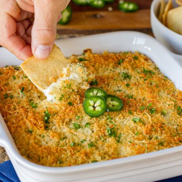 jalapeno popper dip being scooped out of a ceramic baking dish with a pita chip