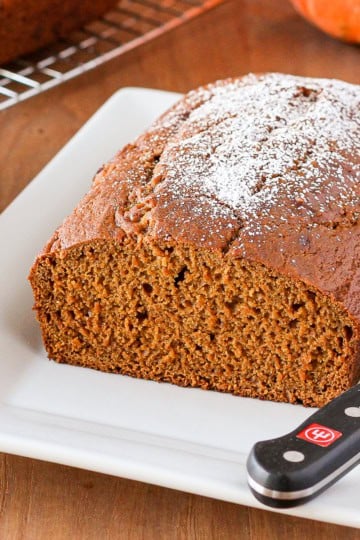 pumpkin bread dusted with powdered sugar on a white ceramic serving platter with a serrated knife on the side