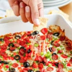 pepperoni pizza dip being scooped out of a dish with a tortilla chip
