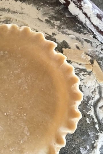 pie crust recipe using crisco dough in a pie plate with crimped edges and flour sprinkled around