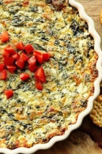 olive garden spinach artichoke dip in a baking dish garnished with diced red peppers