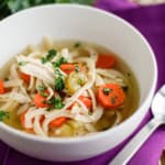 pressure cooker chicken noodle soup in a white bowl with a purple napkin