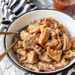 juicy and tender instant pot pulled pork in a black and white enamelware bowl with two forks