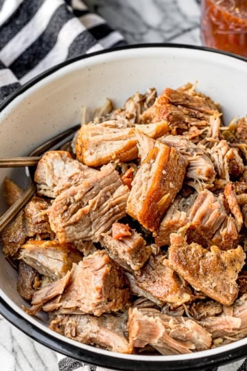 juicy and tender instant pot pulled pork in a black and white enamelware bowl with two forks