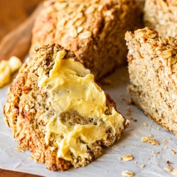 a wedge of lightly sweet irish soda bread with oatmeal and walnuts spread with softened butter