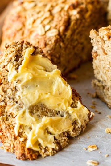 a wedge of lightly sweet irish soda bread with oatmeal and walnuts spread with softened butter